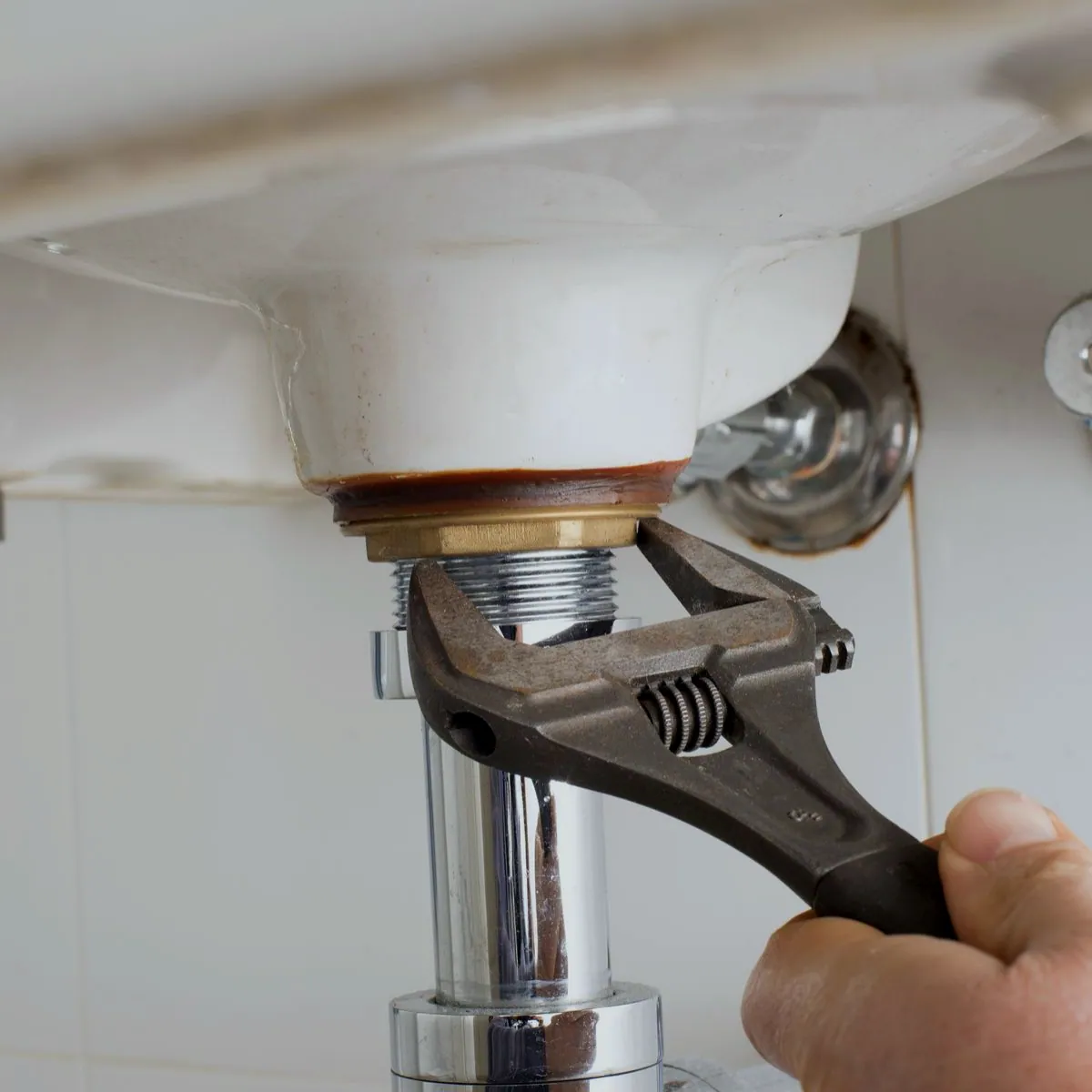Fontanero apretando el desagüe de un lavabo con llave inglesa